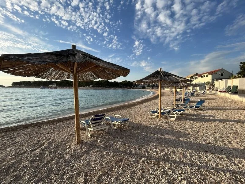 Pebble beach with straw parasols and sun loungers at Camp Adriatic near Primošten