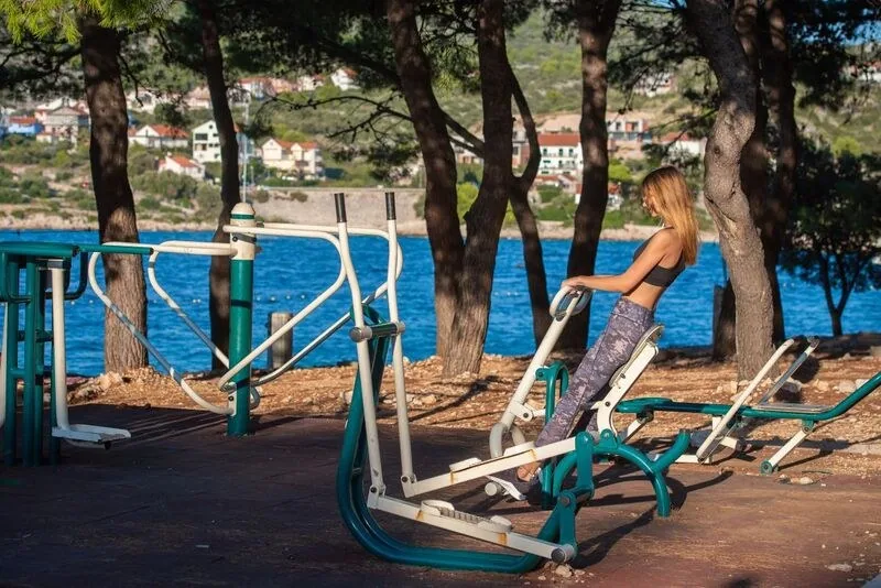 Outdoor fitness equipment beneath pine trees beside the sea at Camp Adriatic