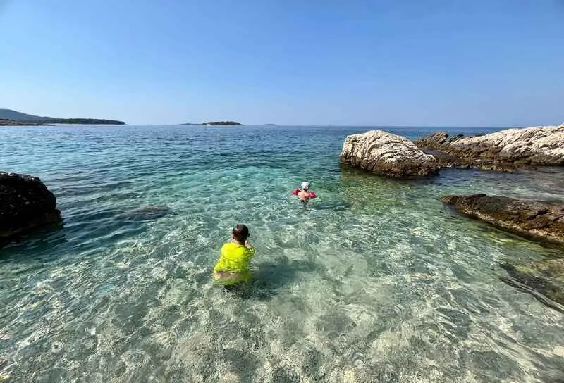 Swimmers in clear shallow water between rocks on the coast near Camp Adriatic